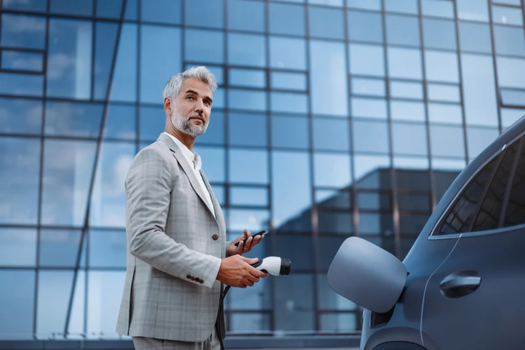 Ein Mann steht neben seinen E-Auto und schließt es zum Aufladen an.