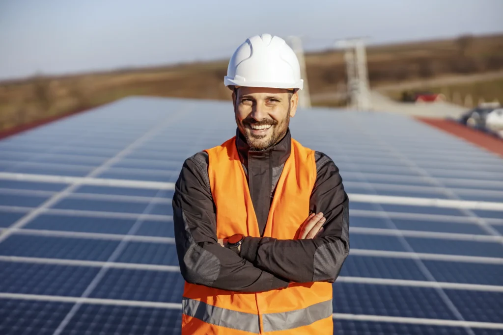 Freundliche lachender Monteur auf einem Dach vor einer Solaranlage.